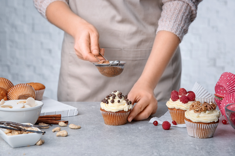 Female,Baker,Decorating,Tasty,Cupcake,With,Cinnamon,At,Table