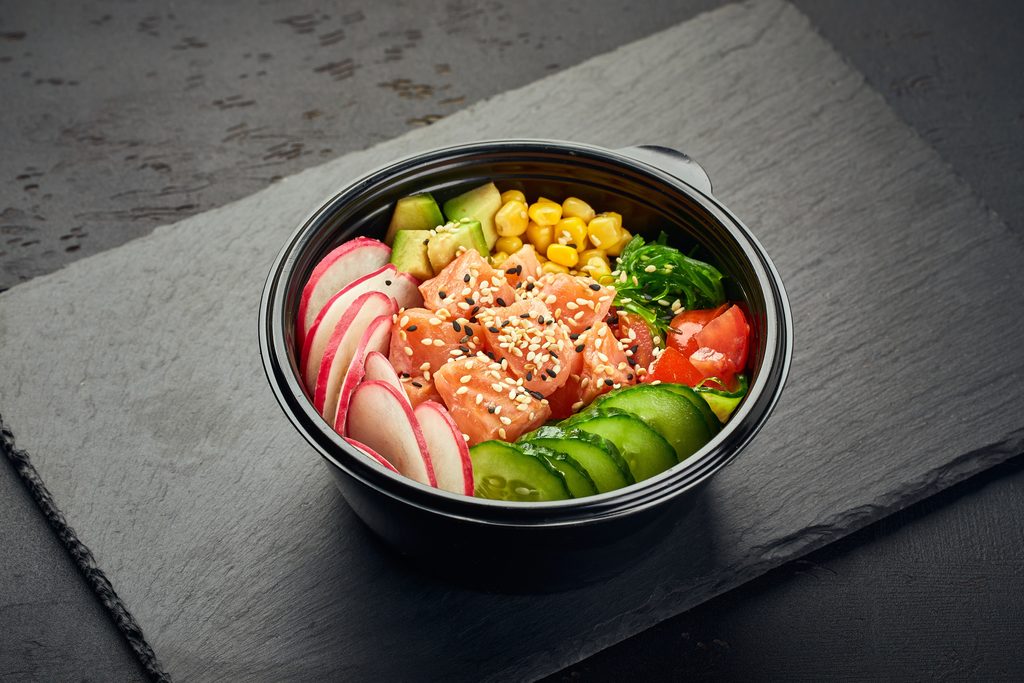 Poke bowl with salmon, avocado, radish, cucumber, tomato, sweet corn and chukka salad in plastic bowl