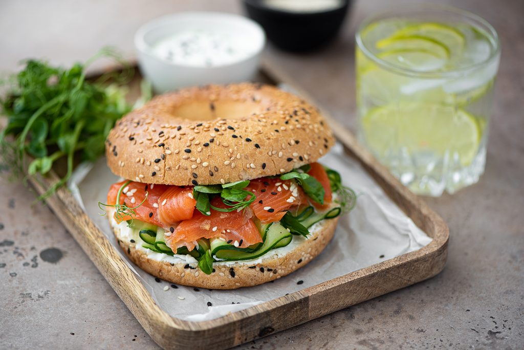 bagel with salted salmon, cucumber and cream cheese on wooden board