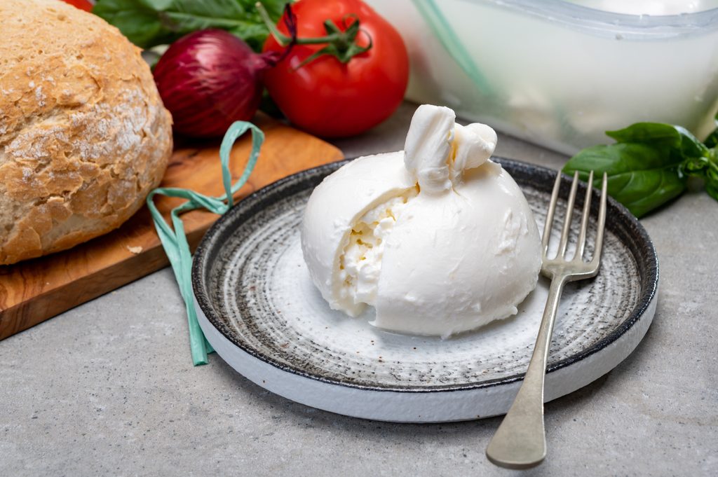 Eating of fresh handmade soft Italian cheese from Puglia, white balls of burrata or burratina cheese made from mozzarella and cream filling close up